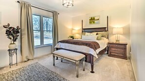 Une chambre à coucher avec un grand lit, des lampes de chevet, un banc, une table de chevet, une fenêtre avec des rideaux et un luminaire au plafond.