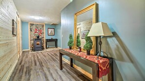 Un couloir doté d’un plancher en bois, d’une cheminée en pierre, d’un miroir et d’une table recouverte d’une nappe rouge.