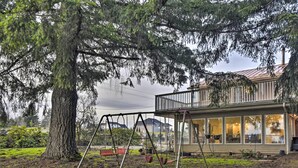 Una propietat residencial amb un gran arbre, un joc de cadira i llisc i una casa amb un balcó.