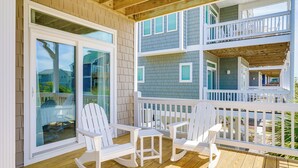 A wooden deck with white rocking chairs and a table, overlooking a residential area. - Modern Surf City Beach House w/ Hot Tub! (Holly Ridge)