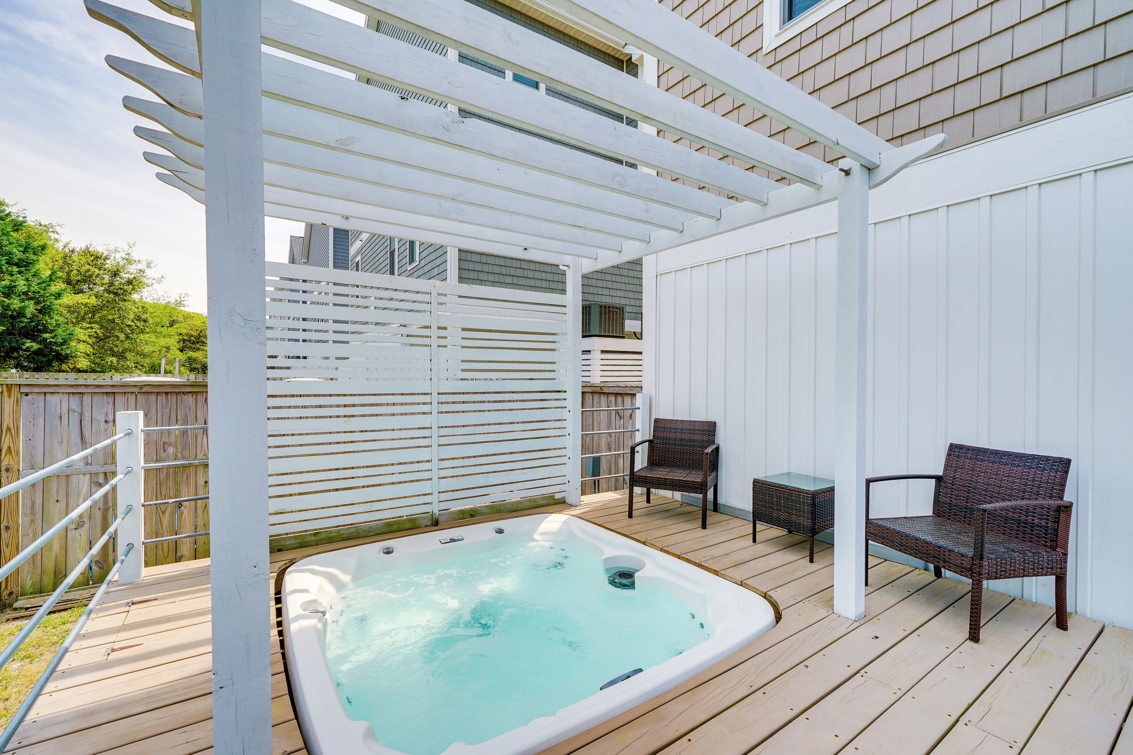 A wooden deck with a hot tub, two wicker chairs, and a pergola structure.