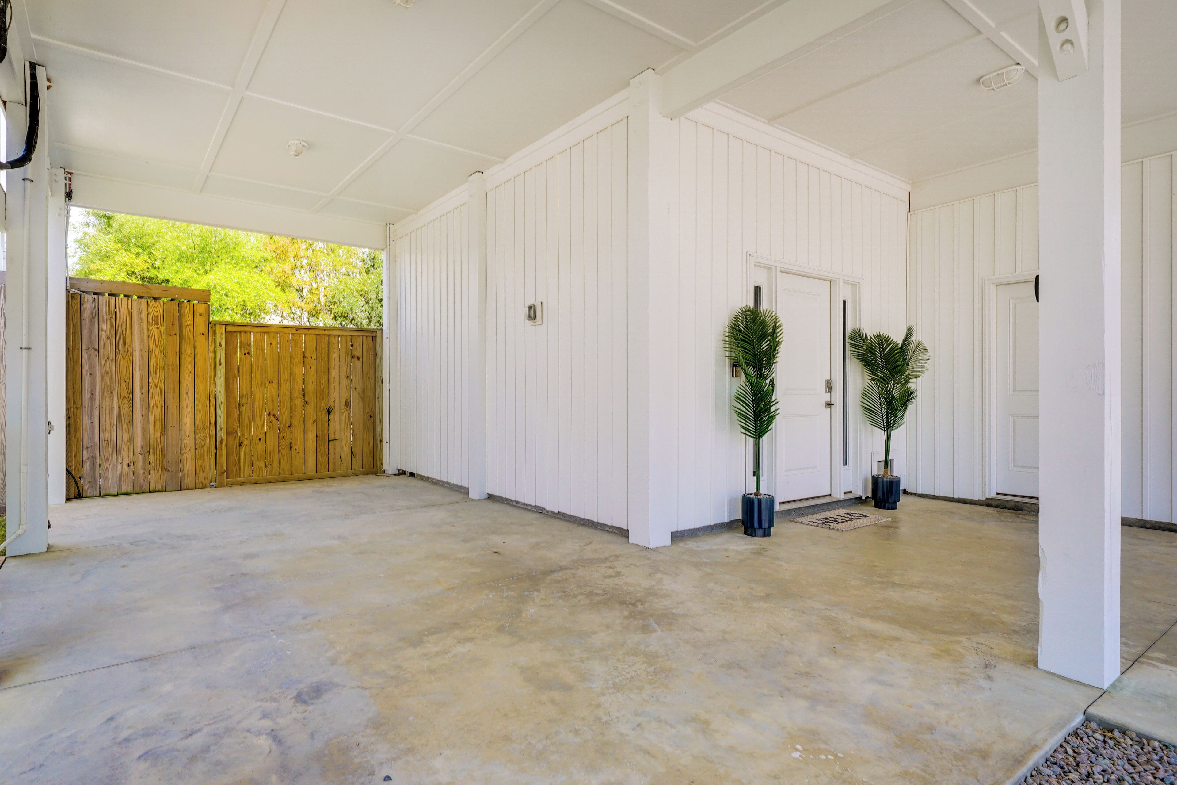 A covered outdoor area with a concrete floor, white walls, and a wooden fence.