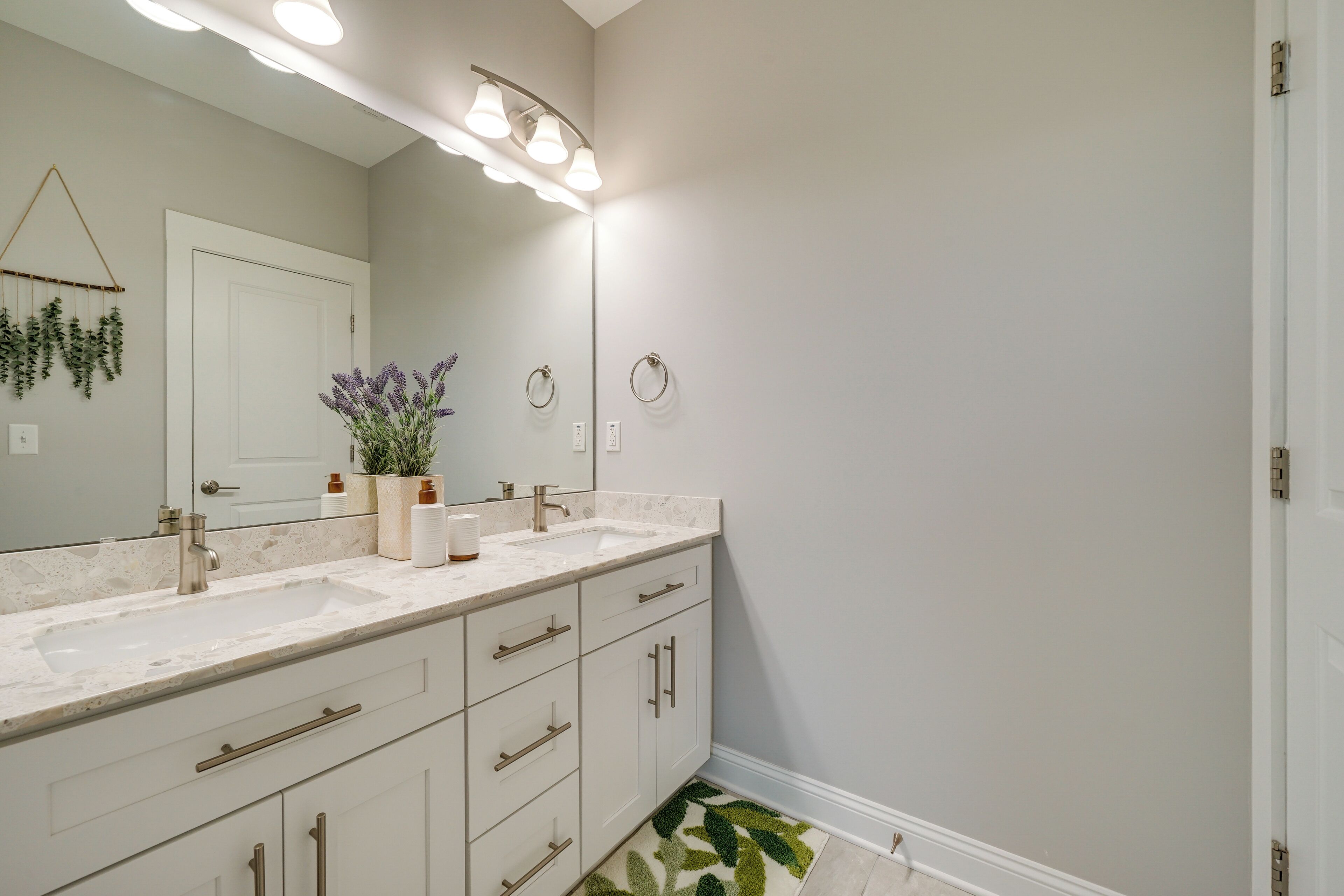 A bathroom with two sinks, a large mirror, and a green leaf-patterned rug.
