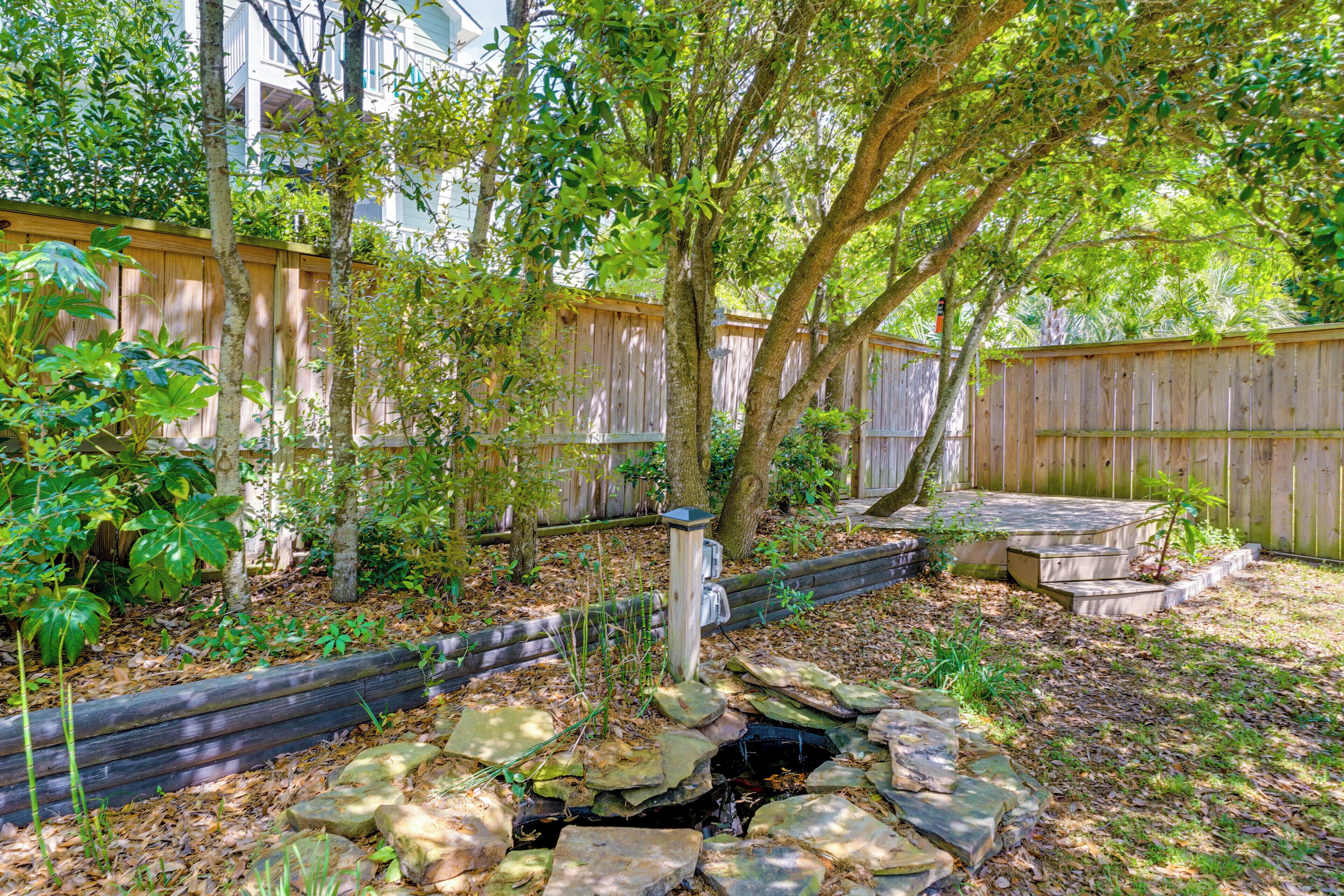 A backyard with a wooden fence, a stone water feature, and various plants.