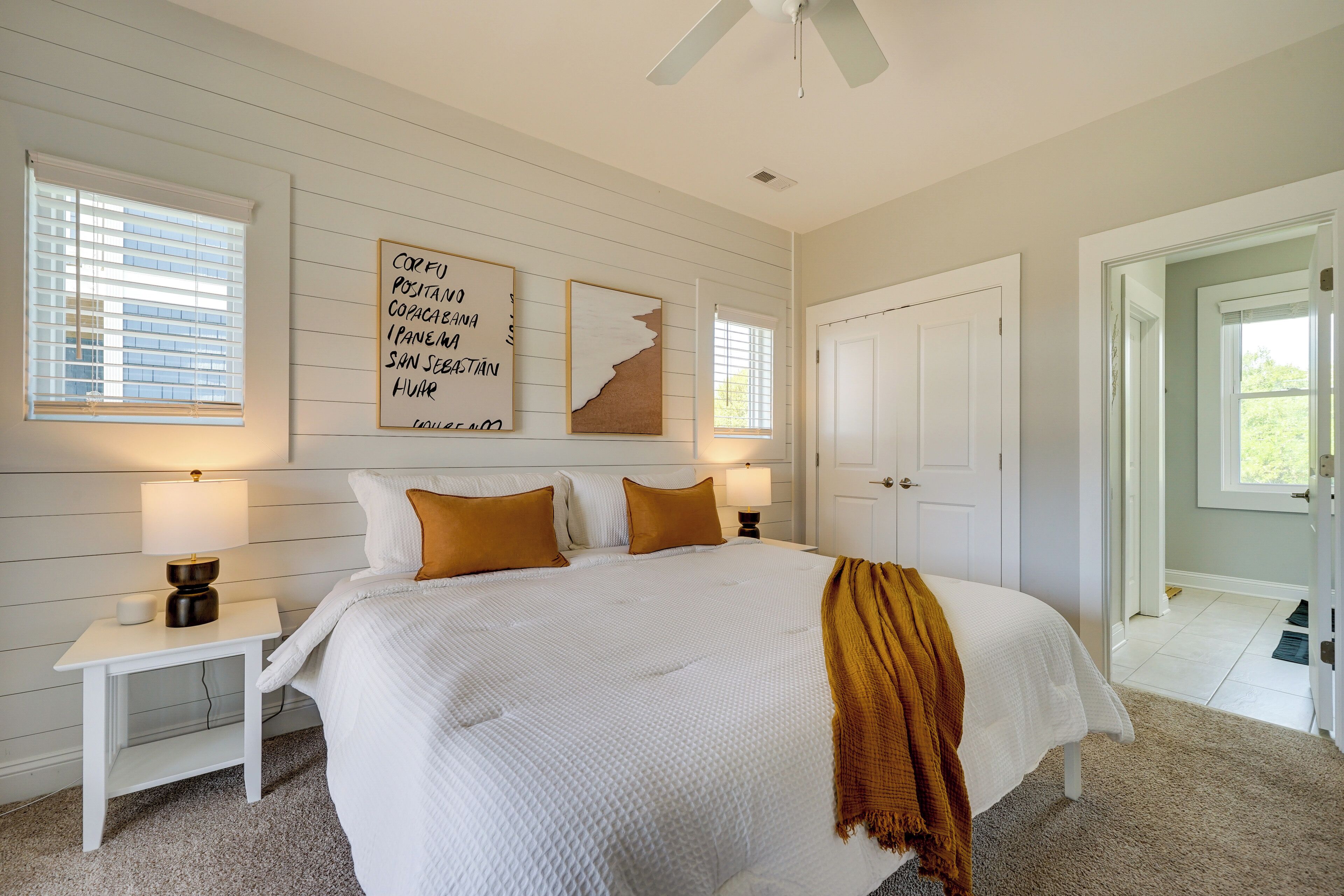 A bedroom with a large bed, white walls, a ceiling fan, and a window with blinds.