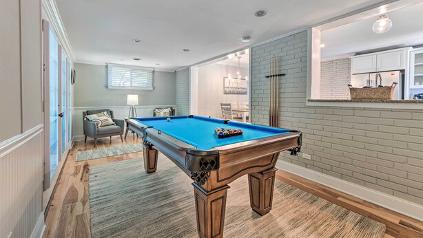 A pool table in a room with a brick wall, a window with blinds, and a door leading to another room.