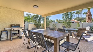 An outdoor patio with a wooden table and chairs, a grill, and a view of palm trees and a house in the background. - Dog-friendly Scottsdale Retreat w/ Private Pool! (Scottsdale)