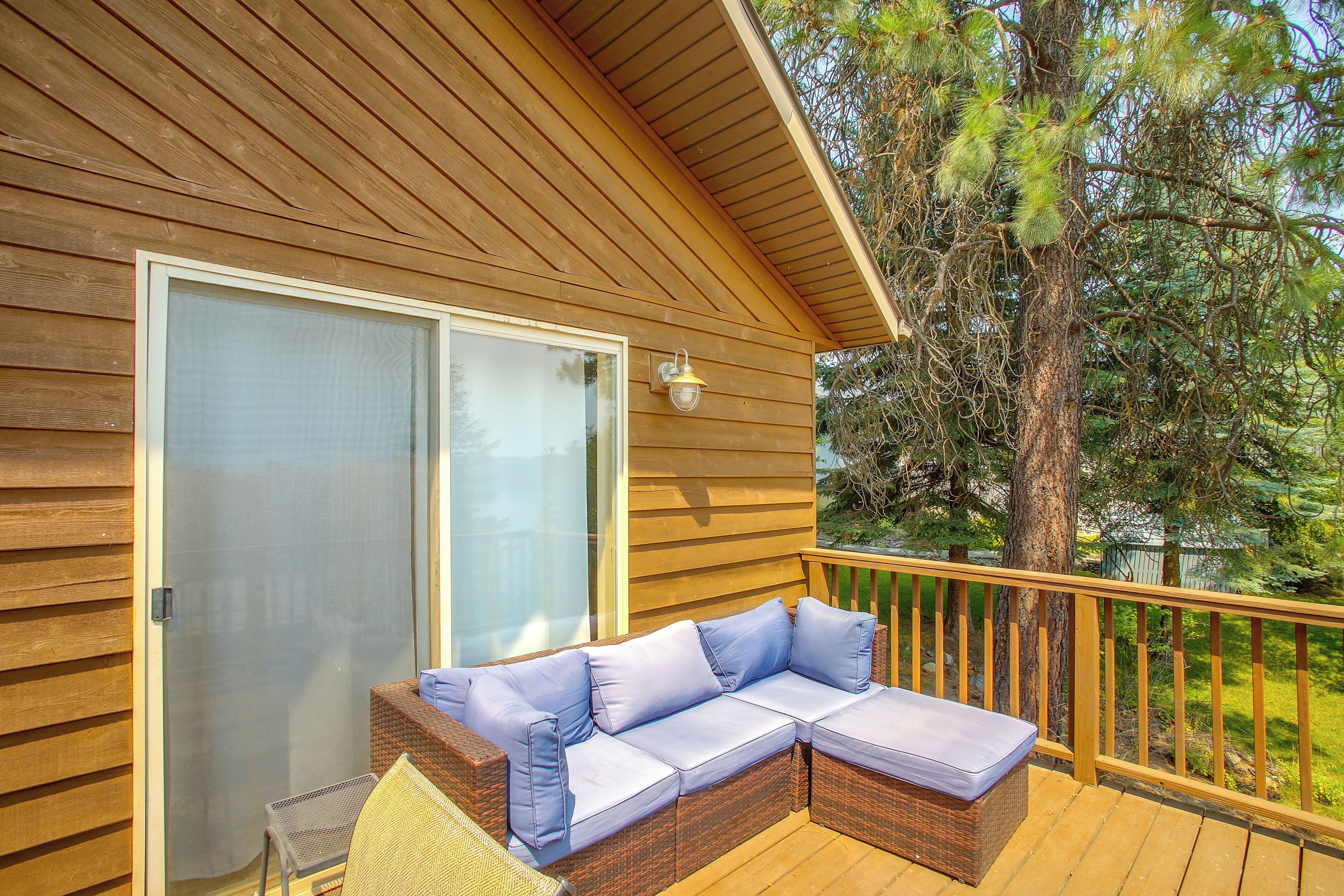 A wooden deck with a wicker sofa and cushions, a sliding glass door, and a wooden railing.