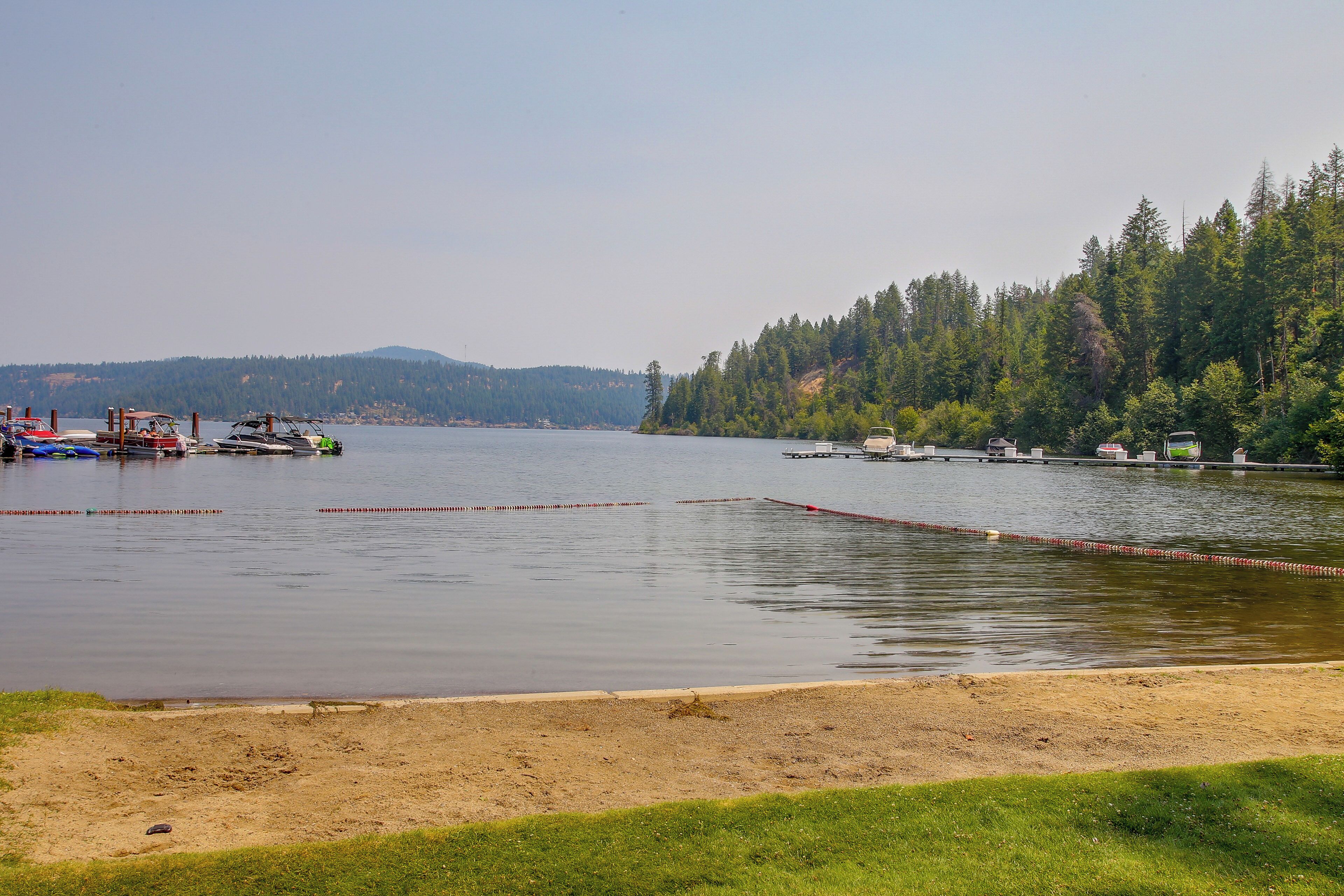 A calm lake with boats docked on the left, surrounded by a forested hillside.