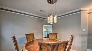 Uma sala de jantar com uma mesa redonda de madeira, cercada por cadeiras, um lustre e um espelho na parede.
