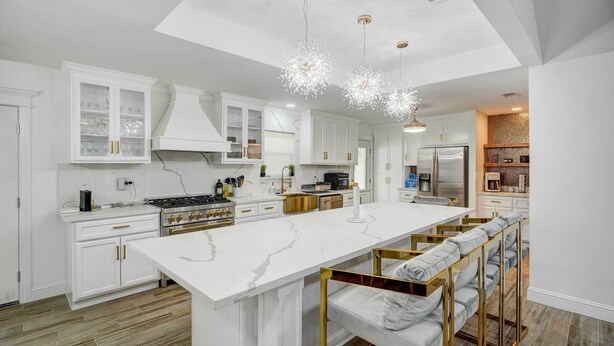 Una cocina moderna con armarios blancos, una isla grande y detalles dorados.