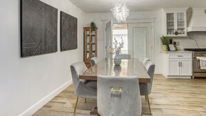 Un comedor moderno con una mesa de vidrio, sillas tapizadas en gris y una araña.