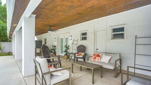 Un patio al aire libre con techo de madera, paredes blancas y un conjunto de asientos que incluye sillas y un sofá.