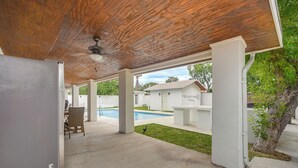 Un área de patio techada con piscina, piso de concreto y ventilador de techo.