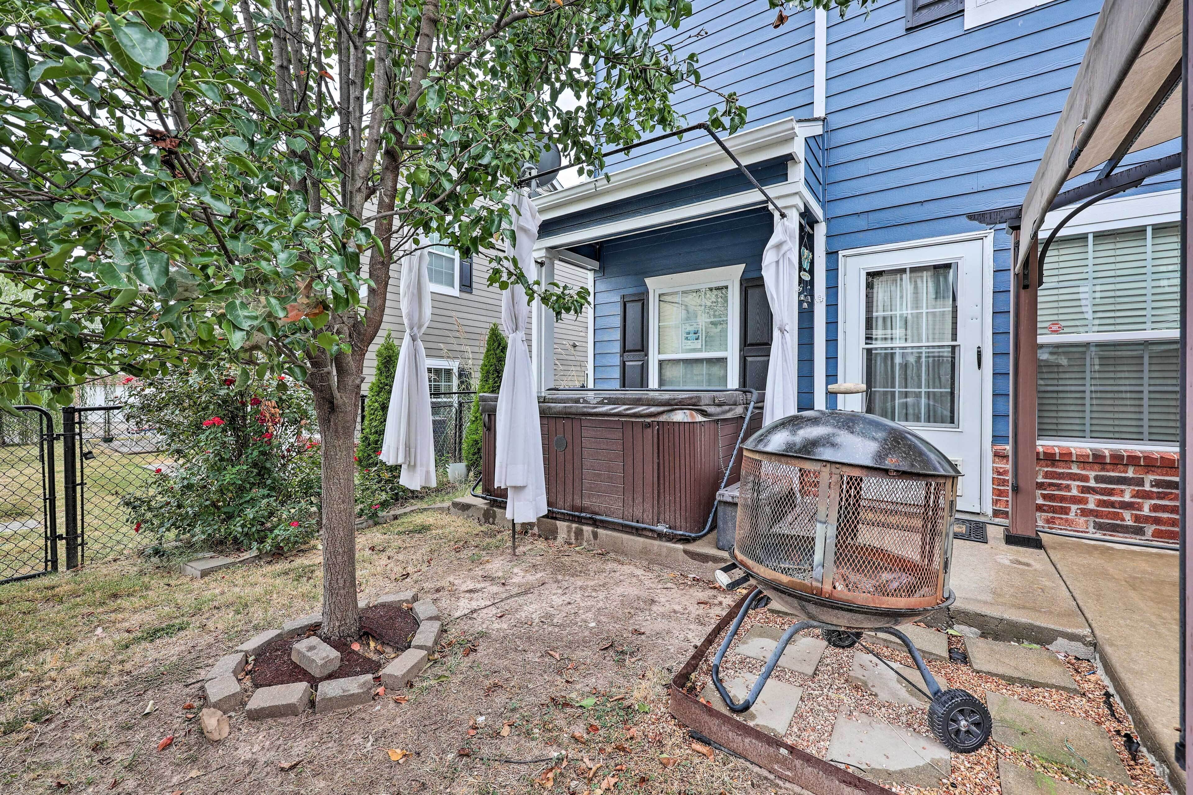 A backyard with a tree, a hot tub, and a grill.