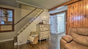 A staircase with a wooden finish, a white wall with a mirror, a wooden door, and a brown leather sofa. - Cozy Goshen Farmhouse ~ 9 Mi to Amish Acres (Goshen)