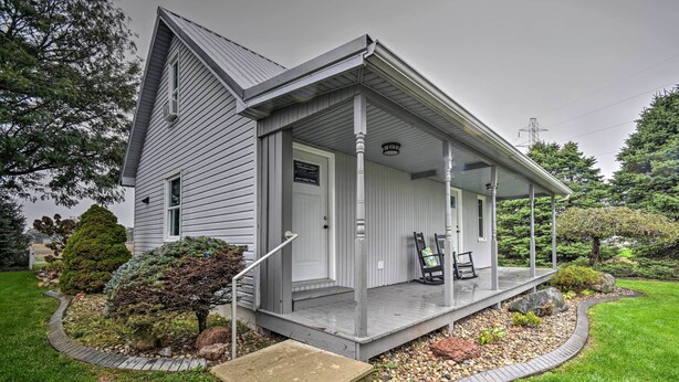 A two-story house with a covered porch, a front door, and a small front yard with a pathway and a few trees. - Cozy Goshen Farmhouse ~ 9 Mi to Amish Acres (Goshen)