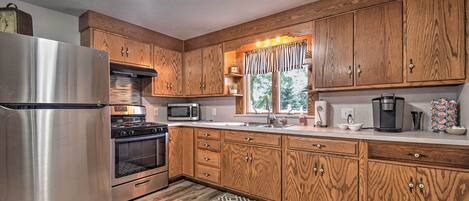 A kitchen with wooden cabinets, stainless steel appliances, a patterned rug, and a window with curtains.