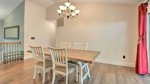 A dining area with a wooden table and white chairs, a chandelier, and a red curtain. - Pet-friendly Mechanicsville Retreat w/ Deck! (Mechanicsville)