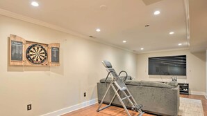 A room with a grey couch, a standing exercise machine, a flat-screen TV, and dartboards on the wall. - Pet-friendly Mechanicsville Retreat w/ Deck! (Mechanicsville)