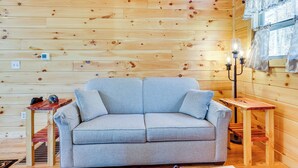 A wooden cabin interior with a grey sofa, a small wooden table, and a lamp. - Stunning Murphy Cabin - 5 Mi to Cherokee Lake! (Murphy)
