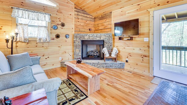 A cozy cabin interior with a stone fireplace, wooden walls, a sofa, and a television mounted on the wall. - Stunning Murphy Cabin - 5 Mi to Cherokee Lake! (Murphy)