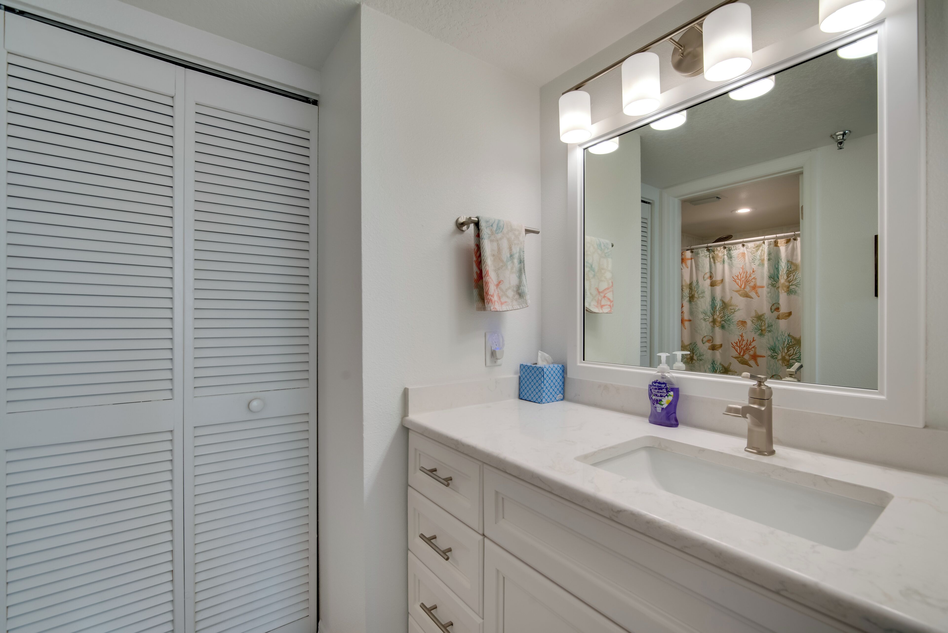 A bathroom with a white vanity, a sink, and a mirror with lights.