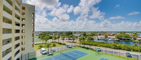 Un court de tennis offrant une vue sur une étendue d’eau et un immeuble à plusieurs étages.