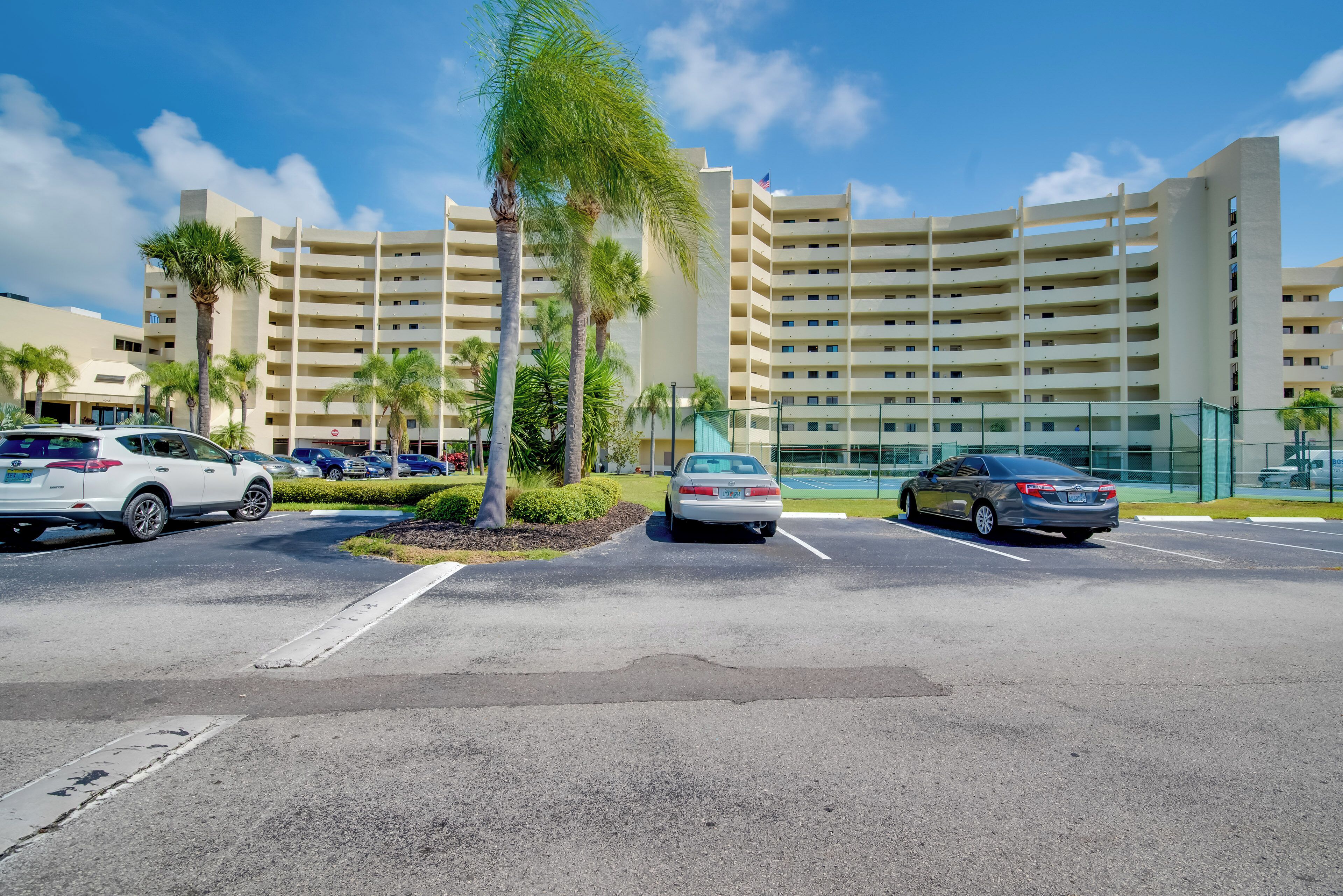 A parking lot with several cars, palm trees, and a multi-story hotel building in the background.