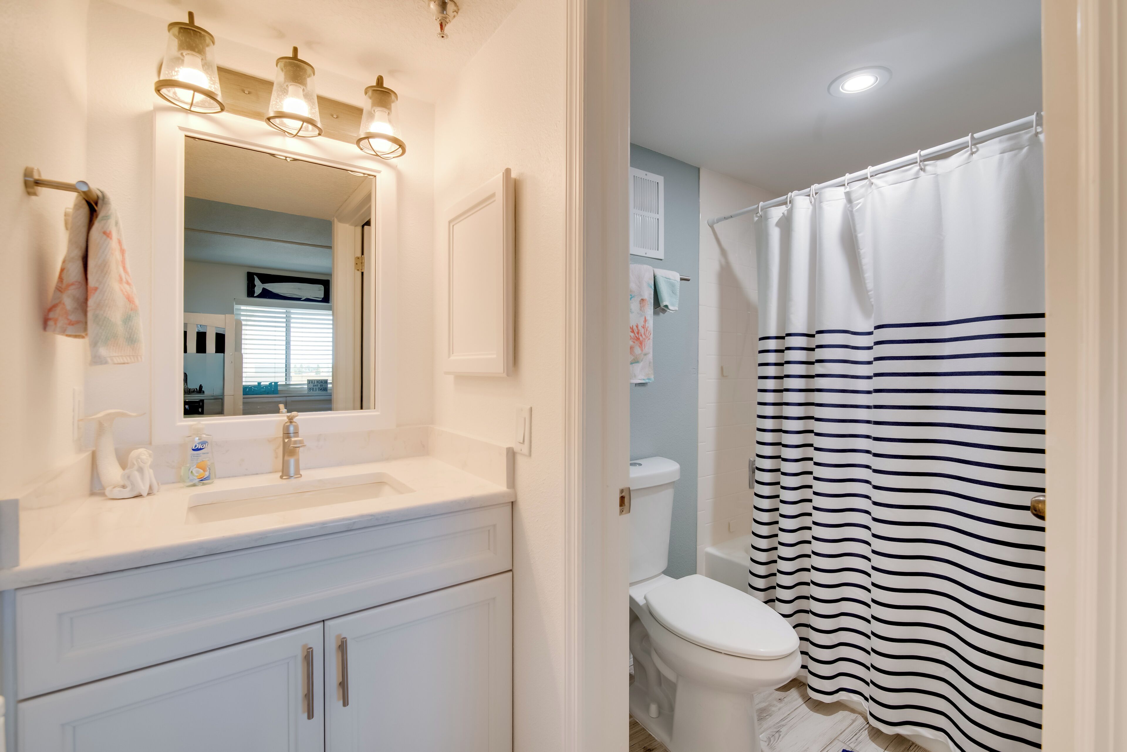 A bathroom with a white vanity, a mirror, and a striped shower curtain.