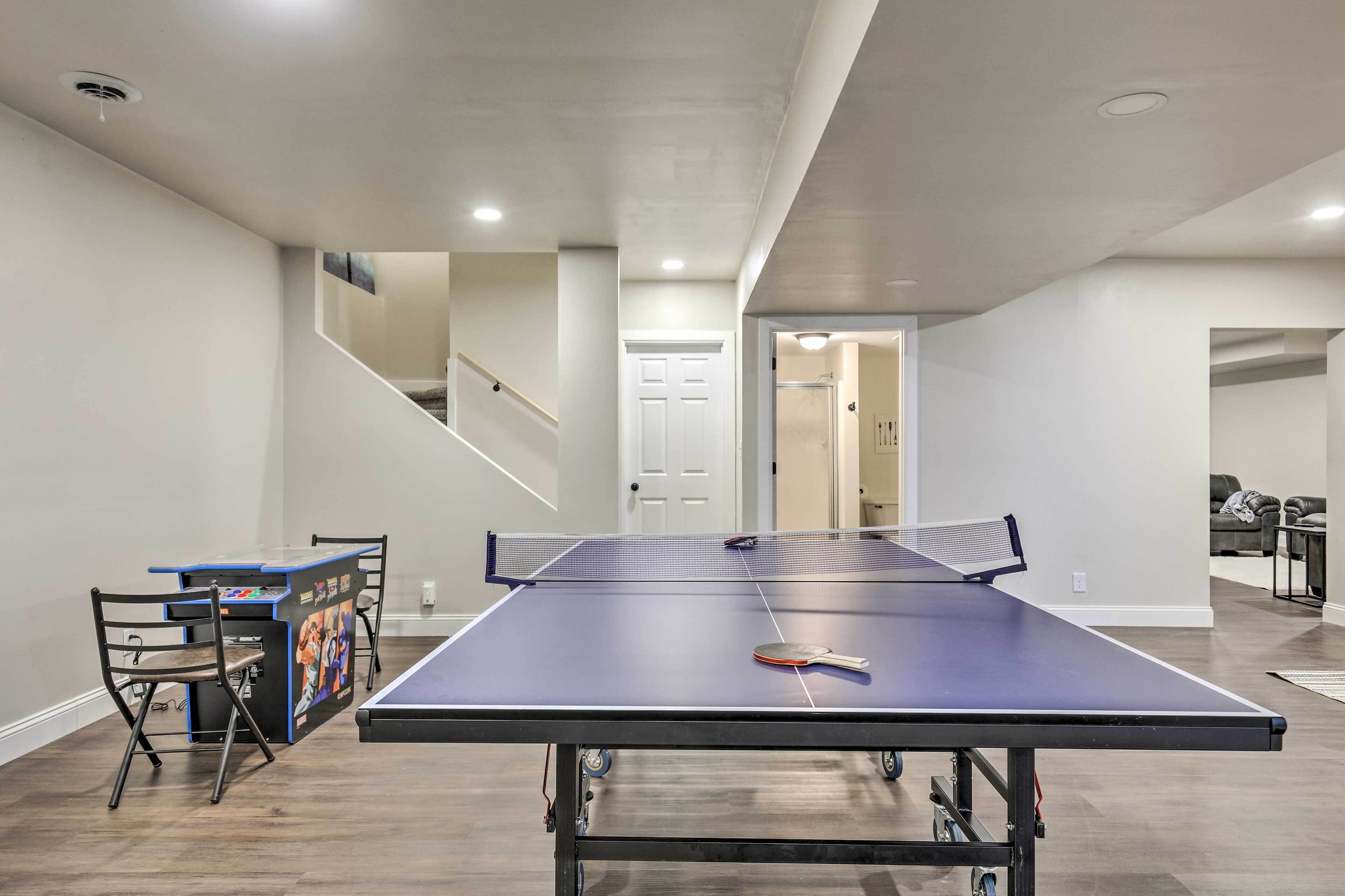Une table de ping-pong dans une pièce avec un escalier, une porte et un canapé à l’arrière-plan.