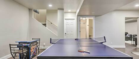 Une table de ping-pong dans une pièce avec un escalier, une porte et un canapé à l’arrière-plan.