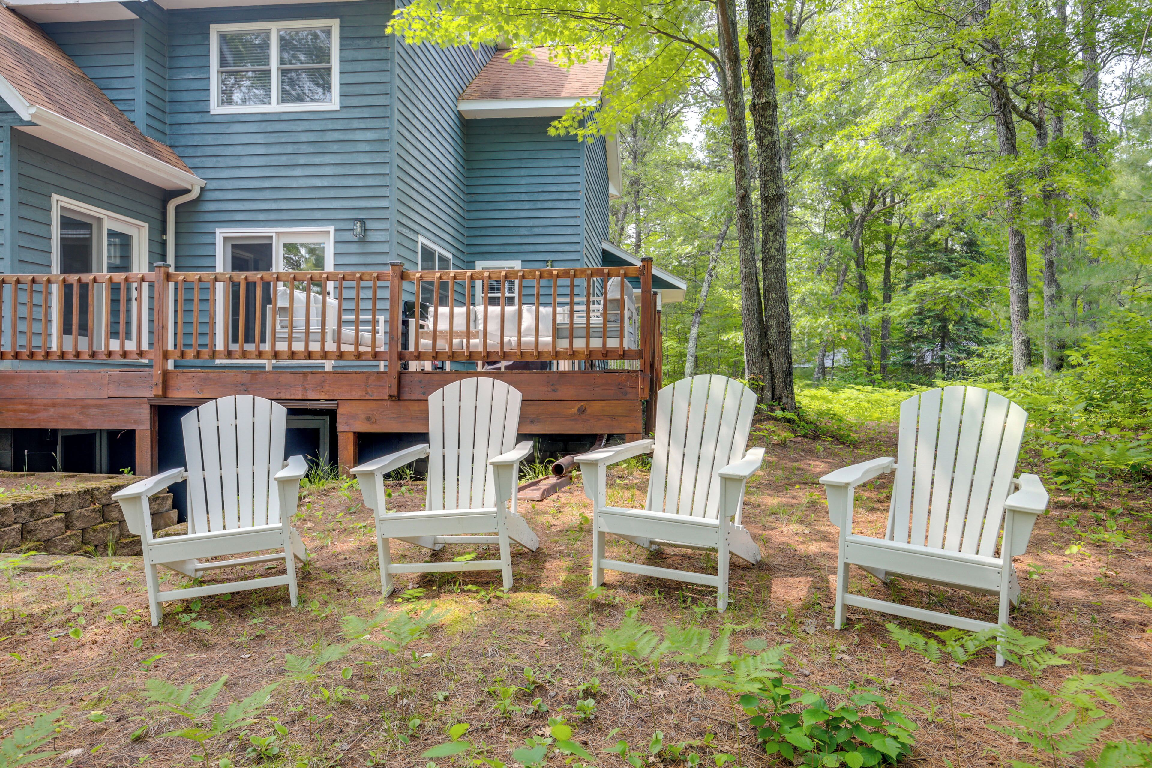 A house with a deck and three Adirondack chairs in front.