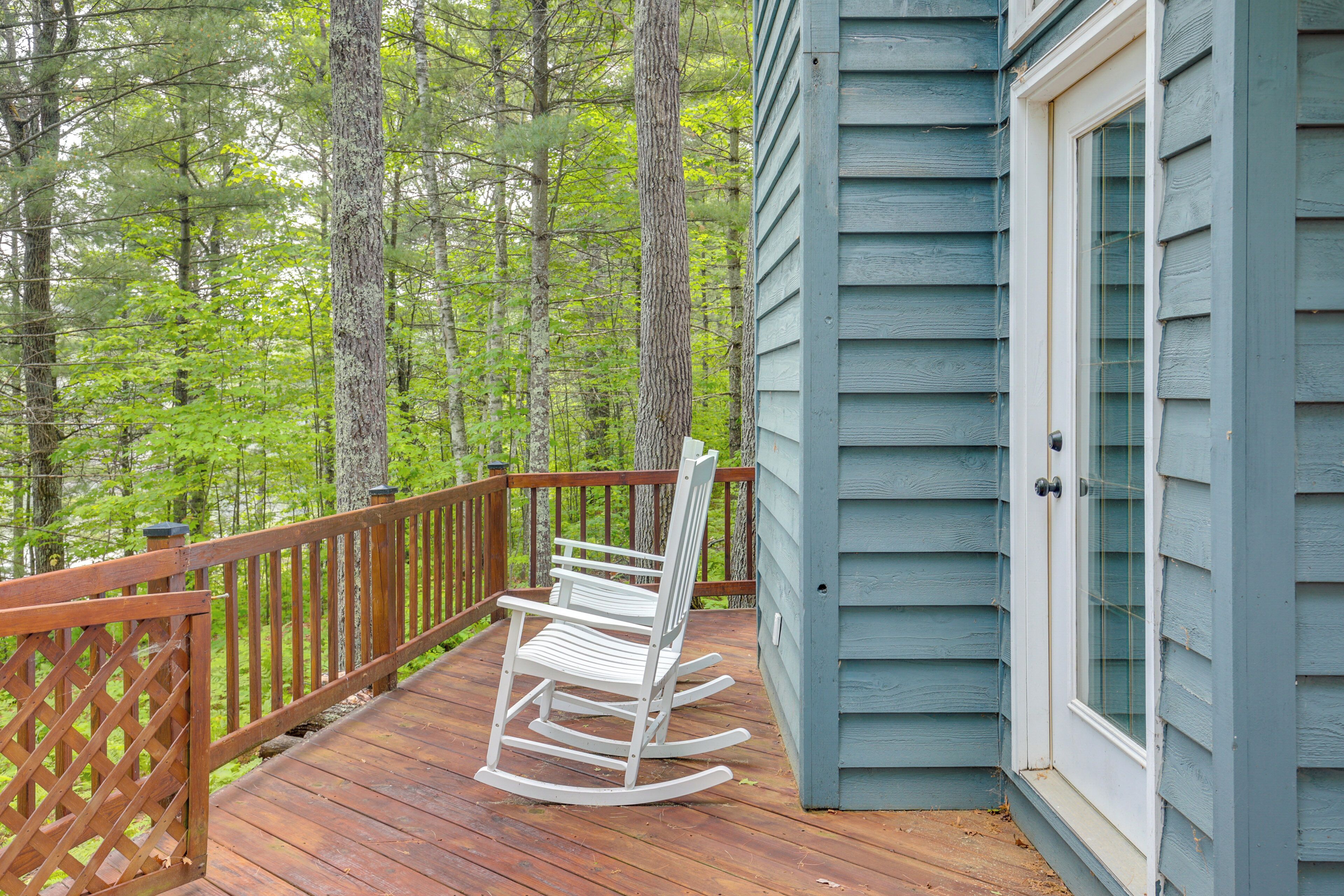 A wooden deck with a rocking chair, surrounded by a wooden railing, and a house with a glass door.