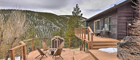 Terraza de madera con mobiliario exterior, jacuzzi y vista a una montaña boscosa.