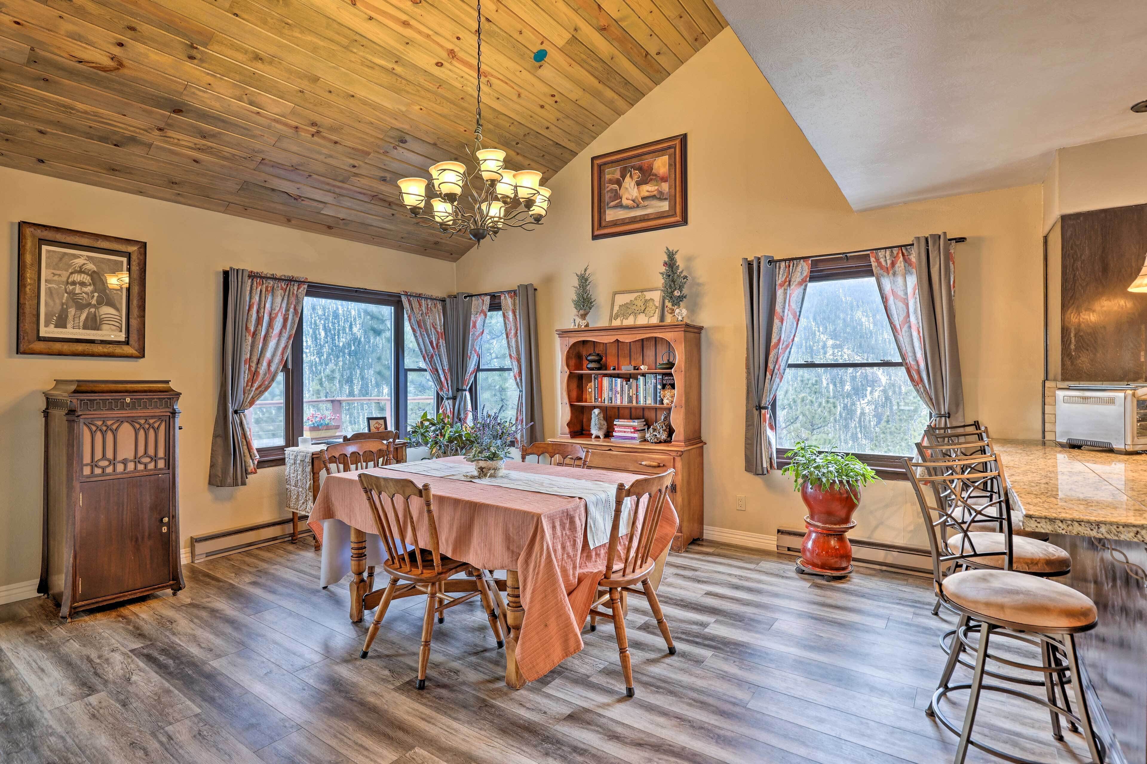 A dining area with a wooden table, chairs, a chandelier, and a bookshelf.