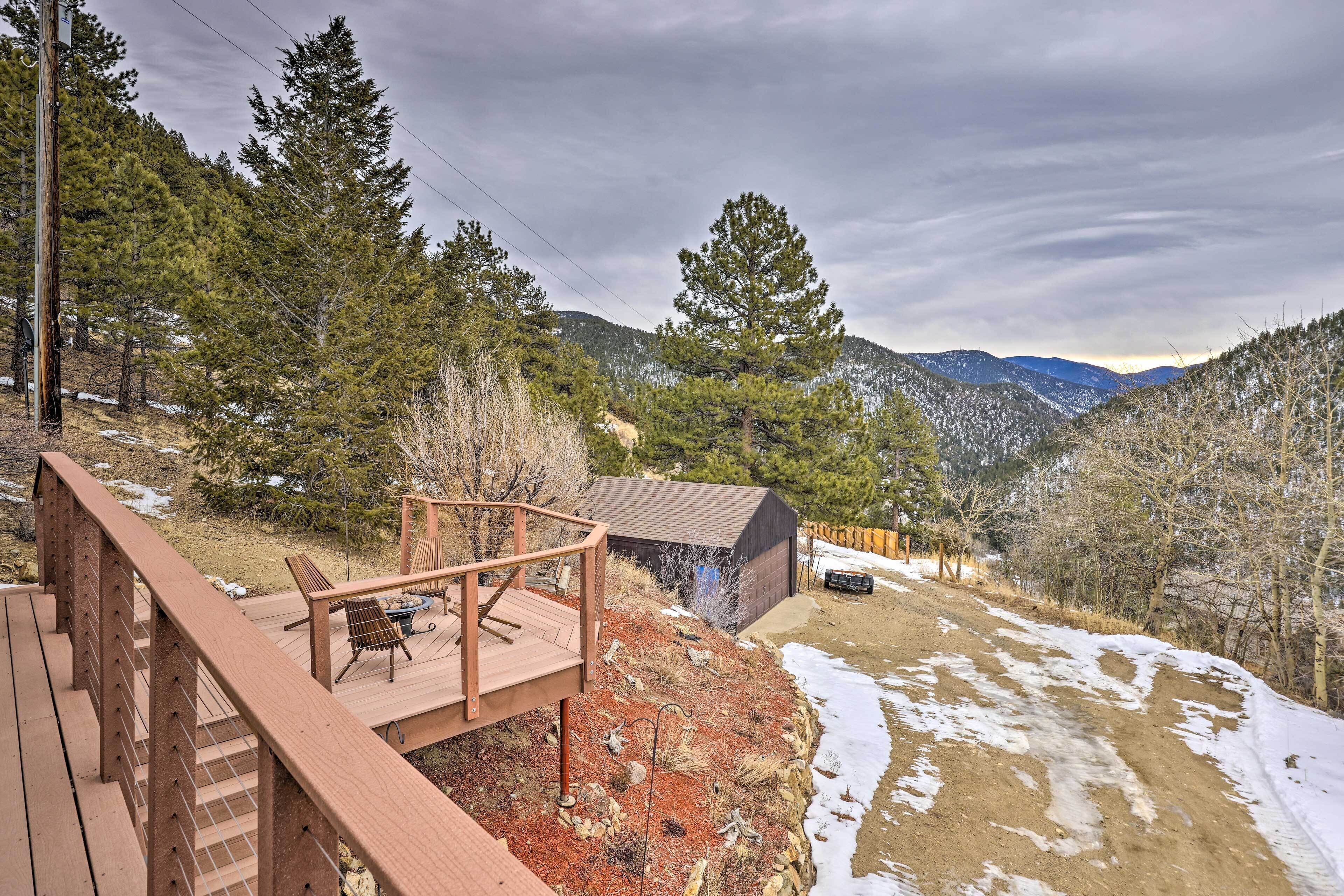 A wooden deck with outdoor seating, a small building, and a mountainous backdrop.