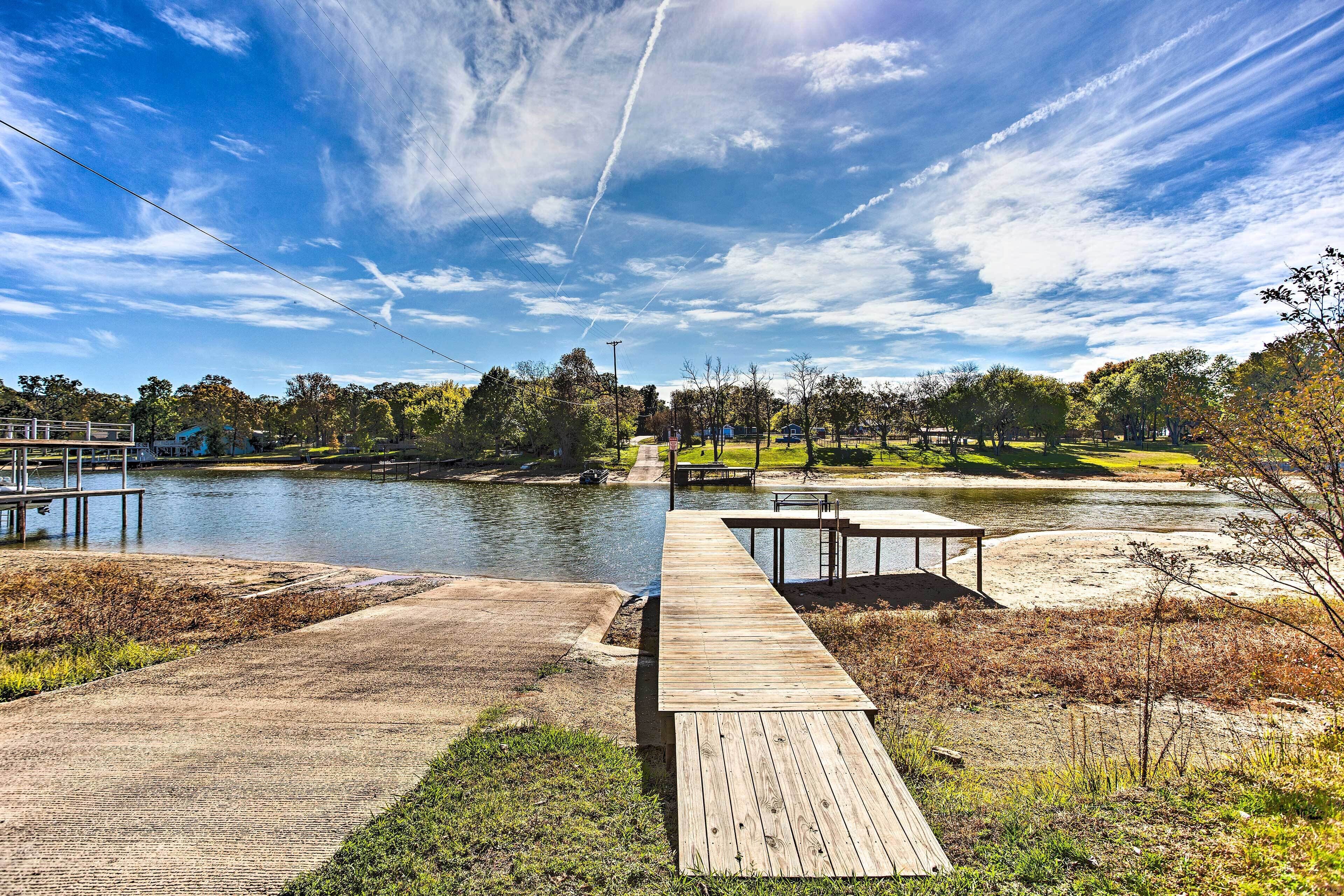 A wooden dock extending over a calm body of water, surrounded by grassy areas and trees.