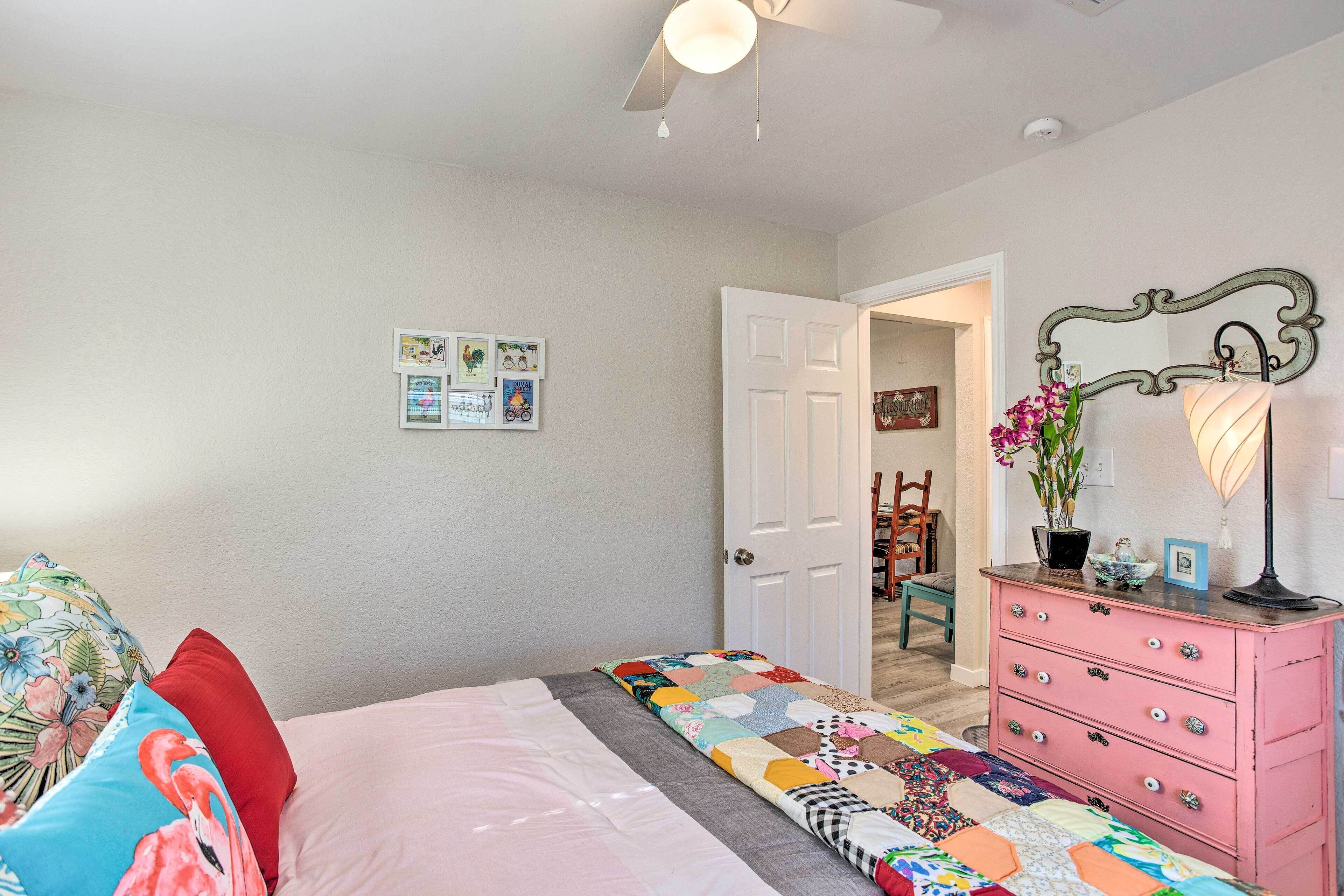 A bedroom with a bed, a dresser, a mirror, and a door leading to another room.