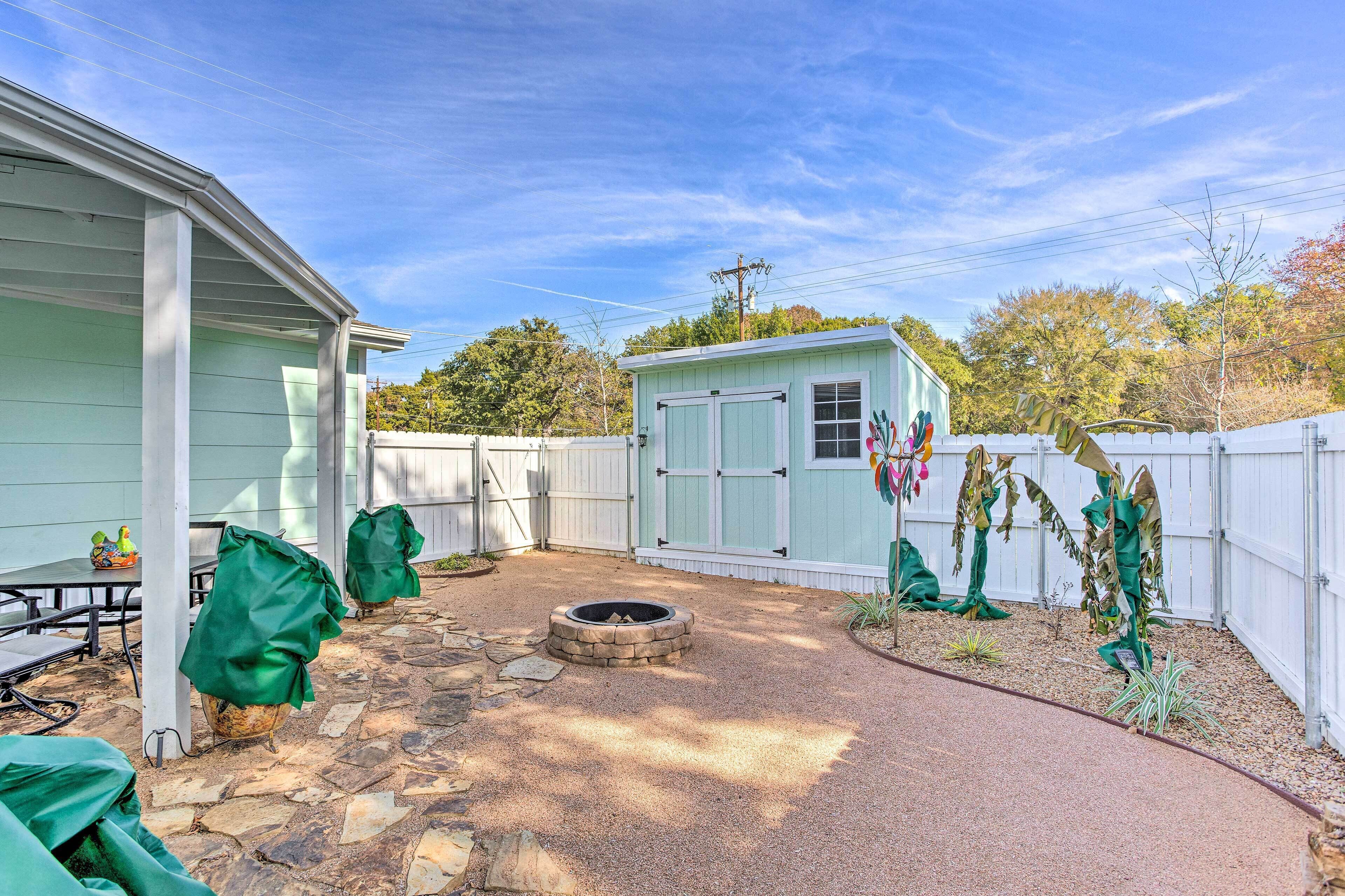 Un jardin avec une terrasse en pierre, un foyer extérieur, un abri de jardin et une table couverte.