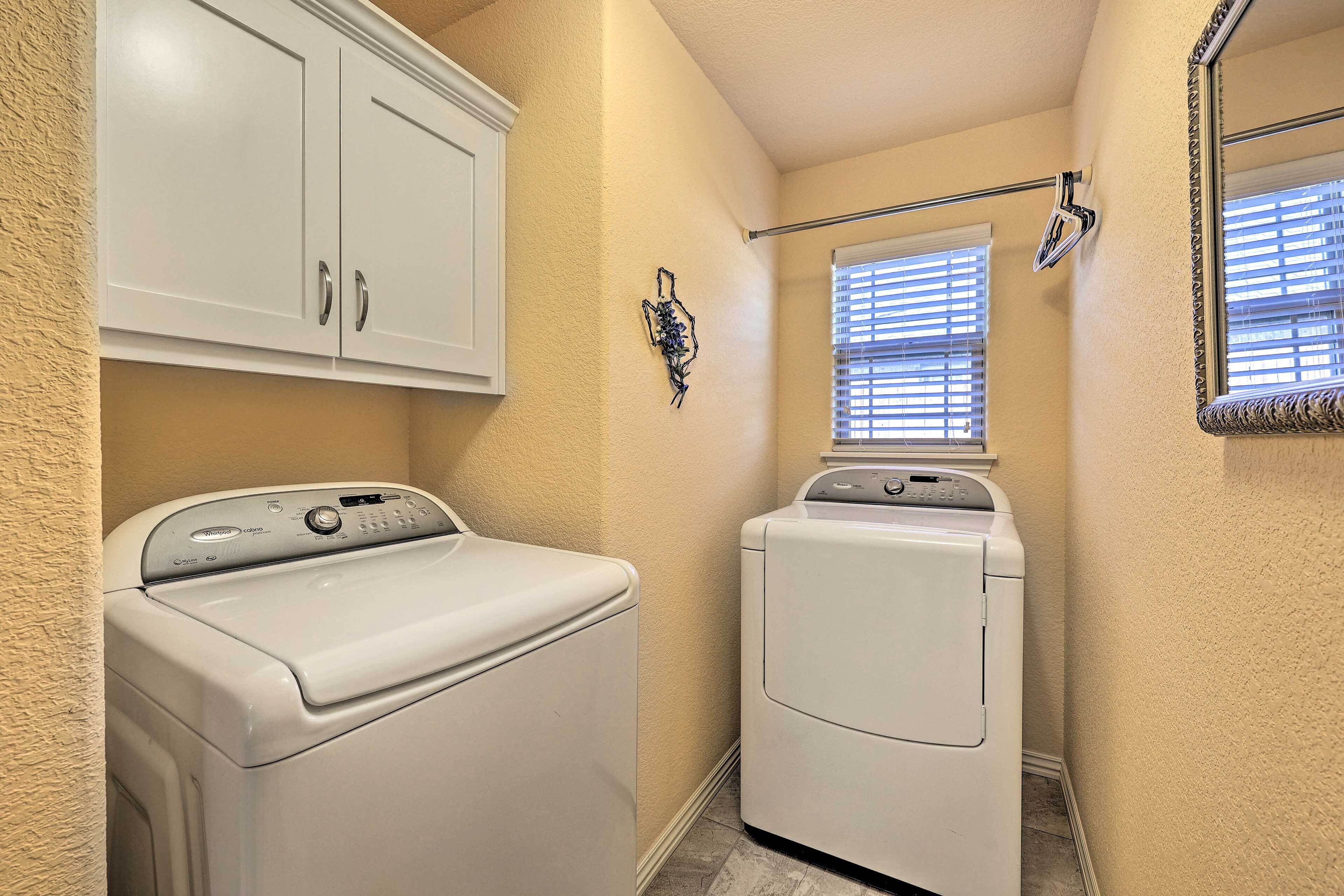 A laundry room with a front-loading washer and dryer, a towel rack, and a window with blinds.