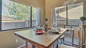 A dining area with a large table set for four, two windows with views of trees, and a small potted plant on the windowsill. - Pet-friendly Prescott Townhome w/ Fireplace! (Prescott)