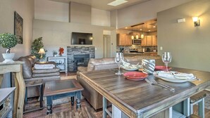 A modern living room with a wooden dining table set for two, leather sofas, a fireplace, and a kitchen in the background. - Pet-friendly Prescott Townhome w/ Fireplace! (Prescott)
