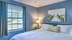 A bedroom with a bed, a window with curtains, a nightstand with a lamp, and a painting on the wall. - Family-friendly New Bern Home w/ Backyard! (New Bern)