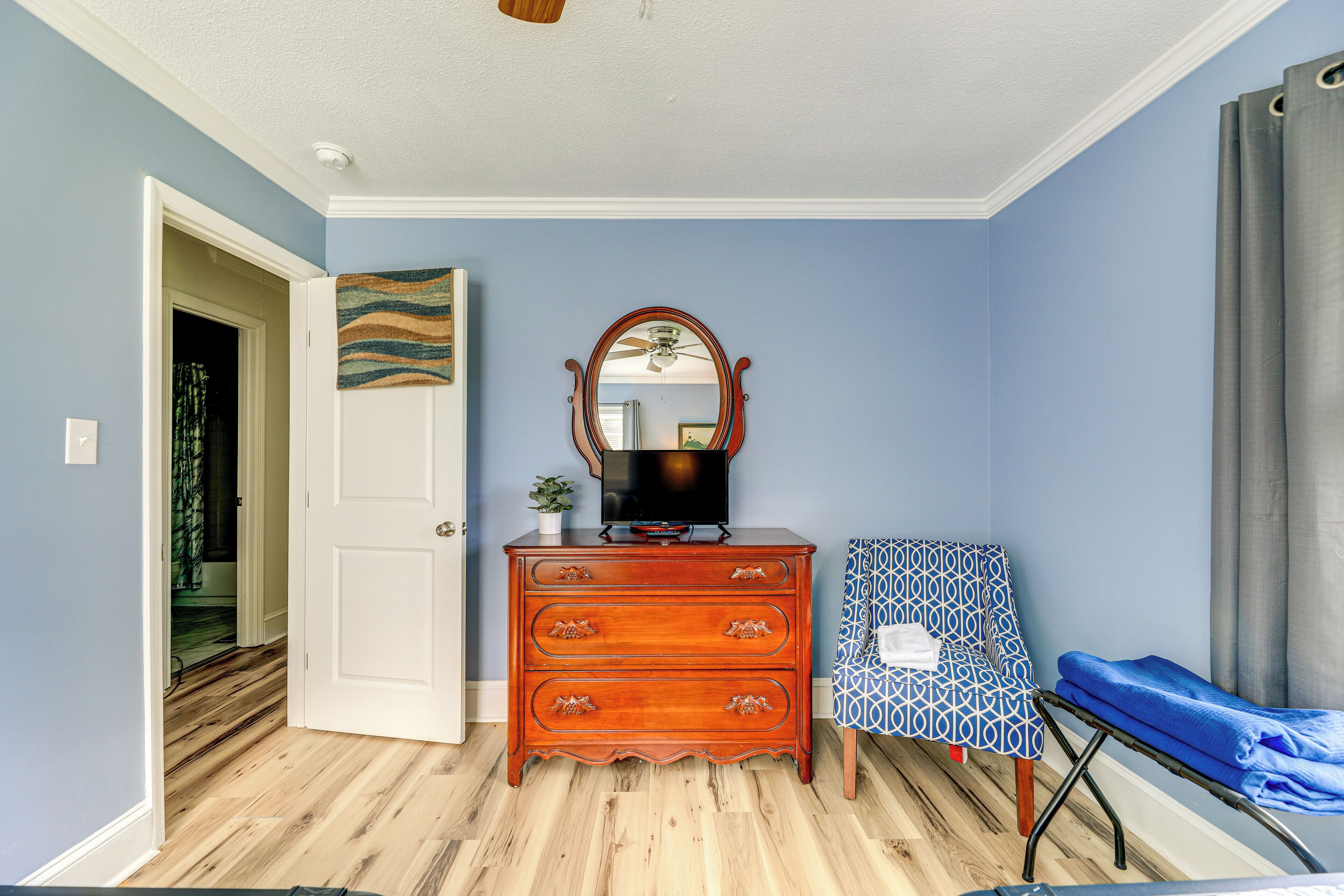 A room with a wooden dresser, a television, a patterned chair, and a blue wall.