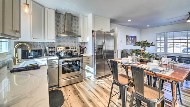 A modern kitchen with stainless steel appliances, a dining area with a wooden table, and a large window providing natural light. - Family-friendly New Bern Home w/ Backyard! (New Bern)