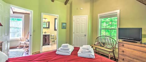 A bedroom with a red bedspread, a wooden dresser, a television, and a window with a view of trees.