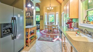 A kitchen with a refrigerator, wooden cabinets, a dining table with chairs, a chandelier, and a stone wall. - 3 Mi to Museums: Smoky Mountains Cabin w/ Deck (Hayesville)