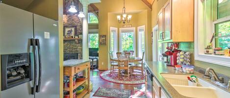 A kitchen with a refrigerator, wooden cabinets, a dining table with chairs, a chandelier, and a stone wall.