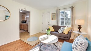 A living room with a sofa, a coffee table, and a lamp. There is a door leading to a kitchen. - Quiet Carpinteria Cottage By Town & Beaches (Carpinteria)